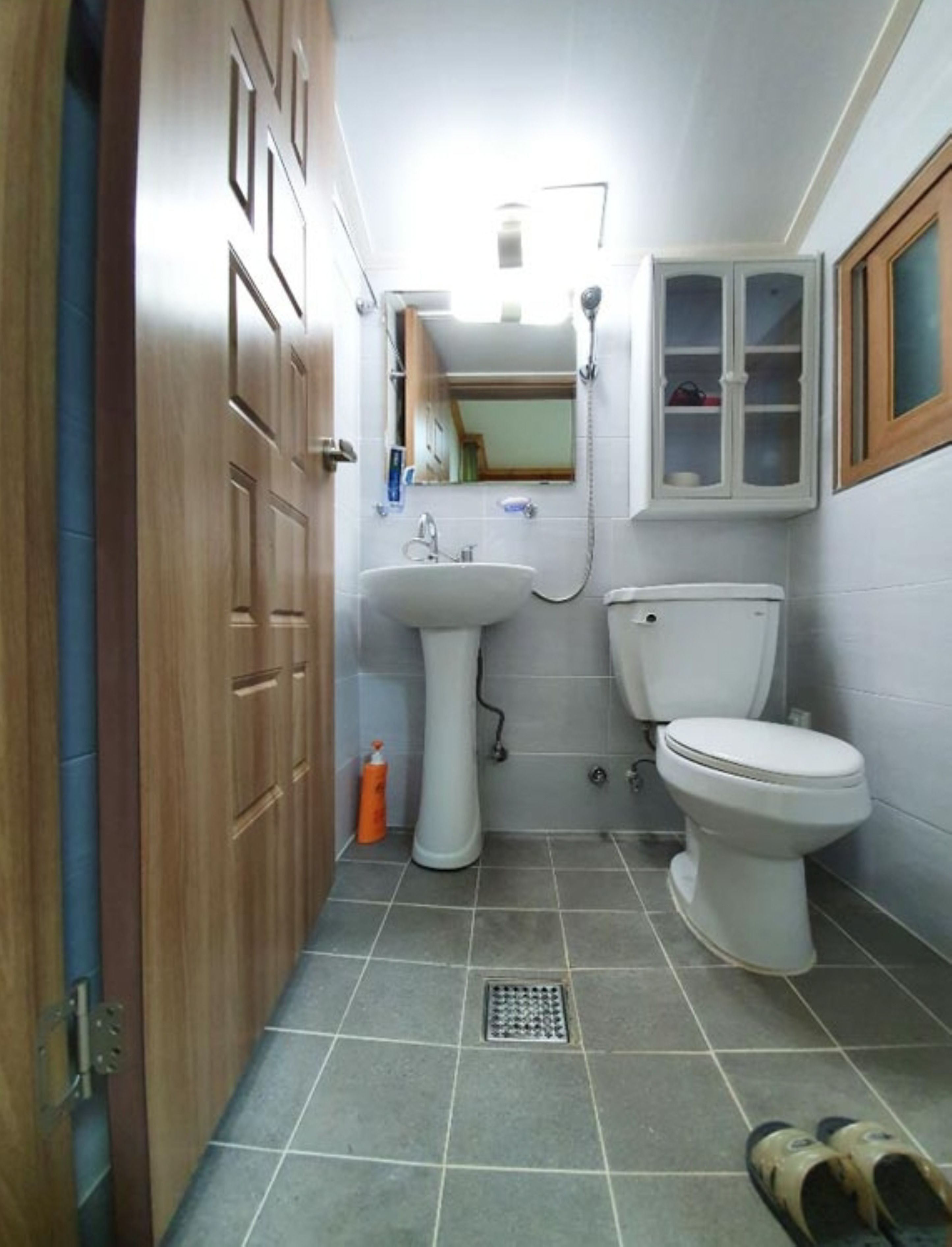 Een kleine badkamer met een wastafel op een zuil, toilet en kast.