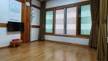 A room with wooden flooring, a flat-screen TV mounted on the wall, a calendar, and a small wooden stool.