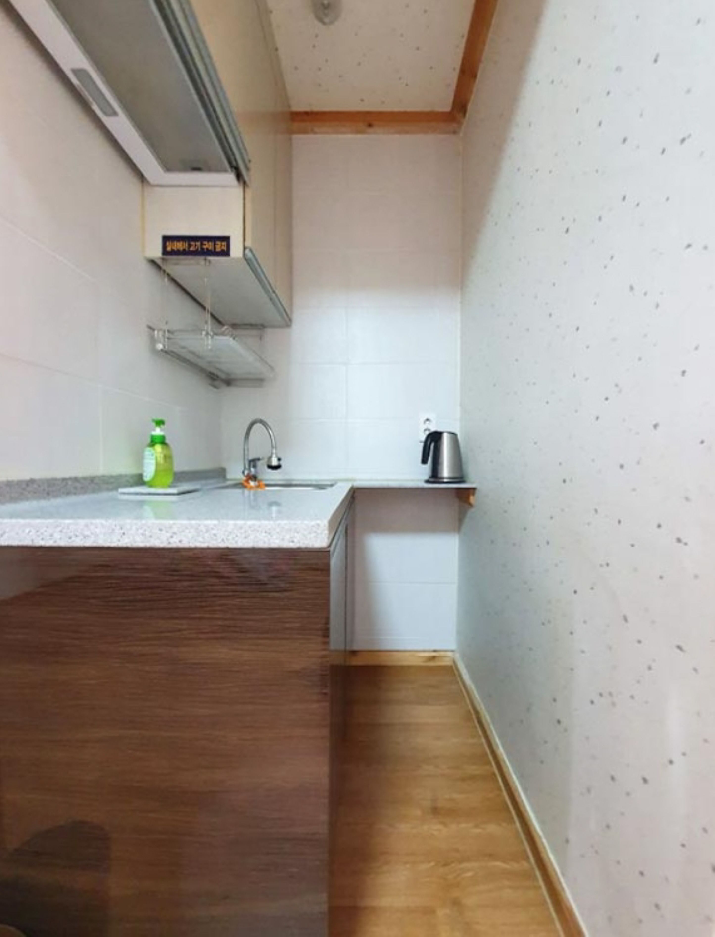 A small kitchen with a wooden countertop, a sink, a kettle, and a bottle of dish soap.