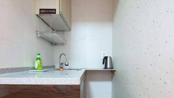 A small kitchen with a wooden countertop, a sink, a kettle, and a bottle of dish soap.