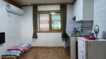 A compact kitchen with a refrigerator, a small sink, and a window with green curtains.