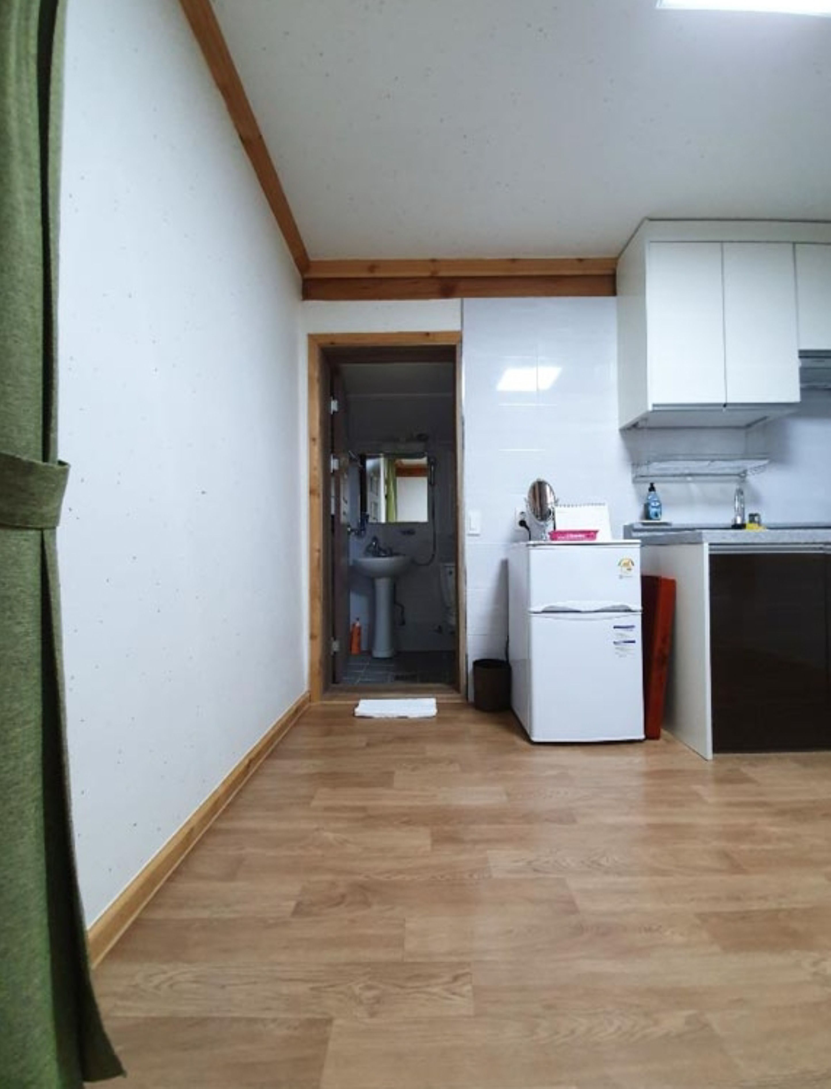 A narrow hallway with wooden flooring leading to a kitchen area with white cabinets and a refrigerator.