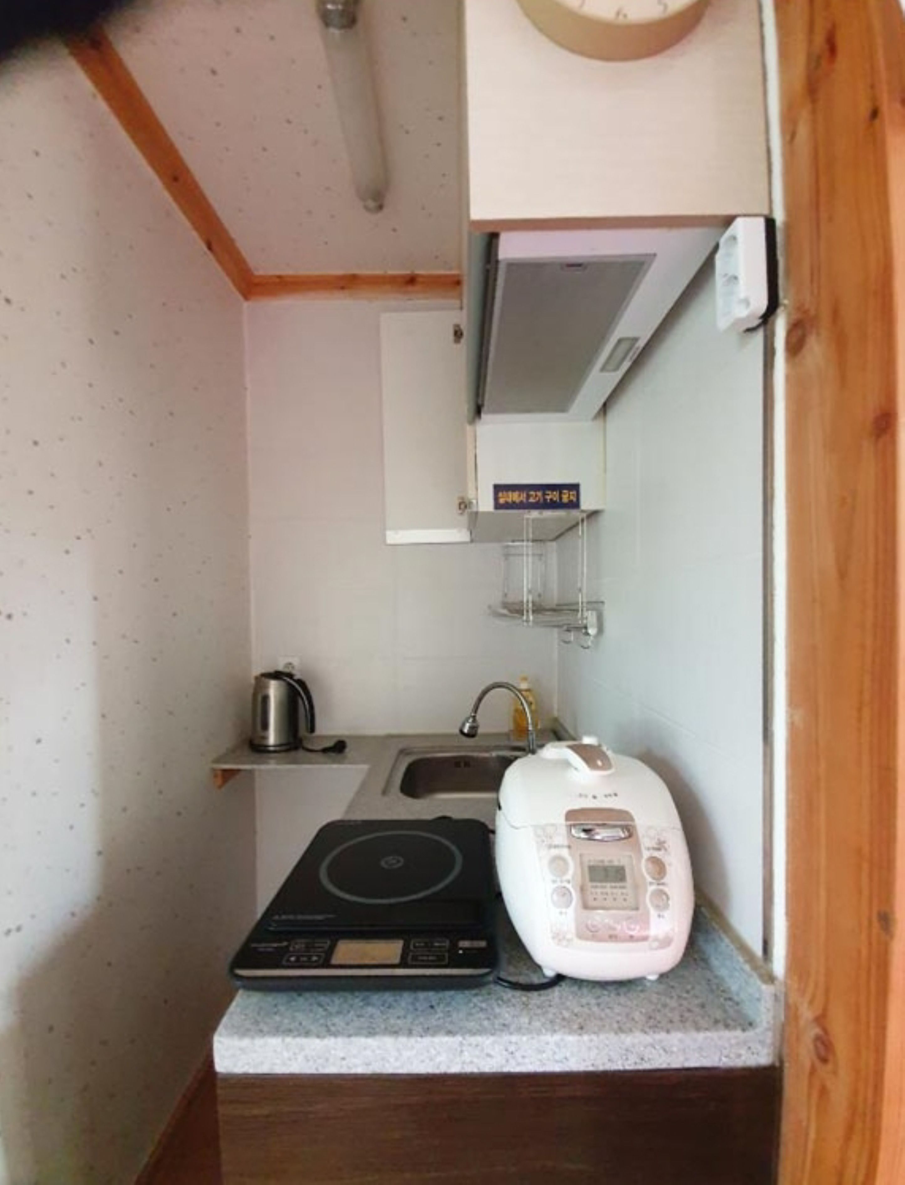 Een compacte keuken met een kookplaat, waterkoker, rijstkoker en magnetron.