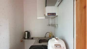 Een compacte keuken met een kookplaat, waterkoker, rijstkoker en magnetron.