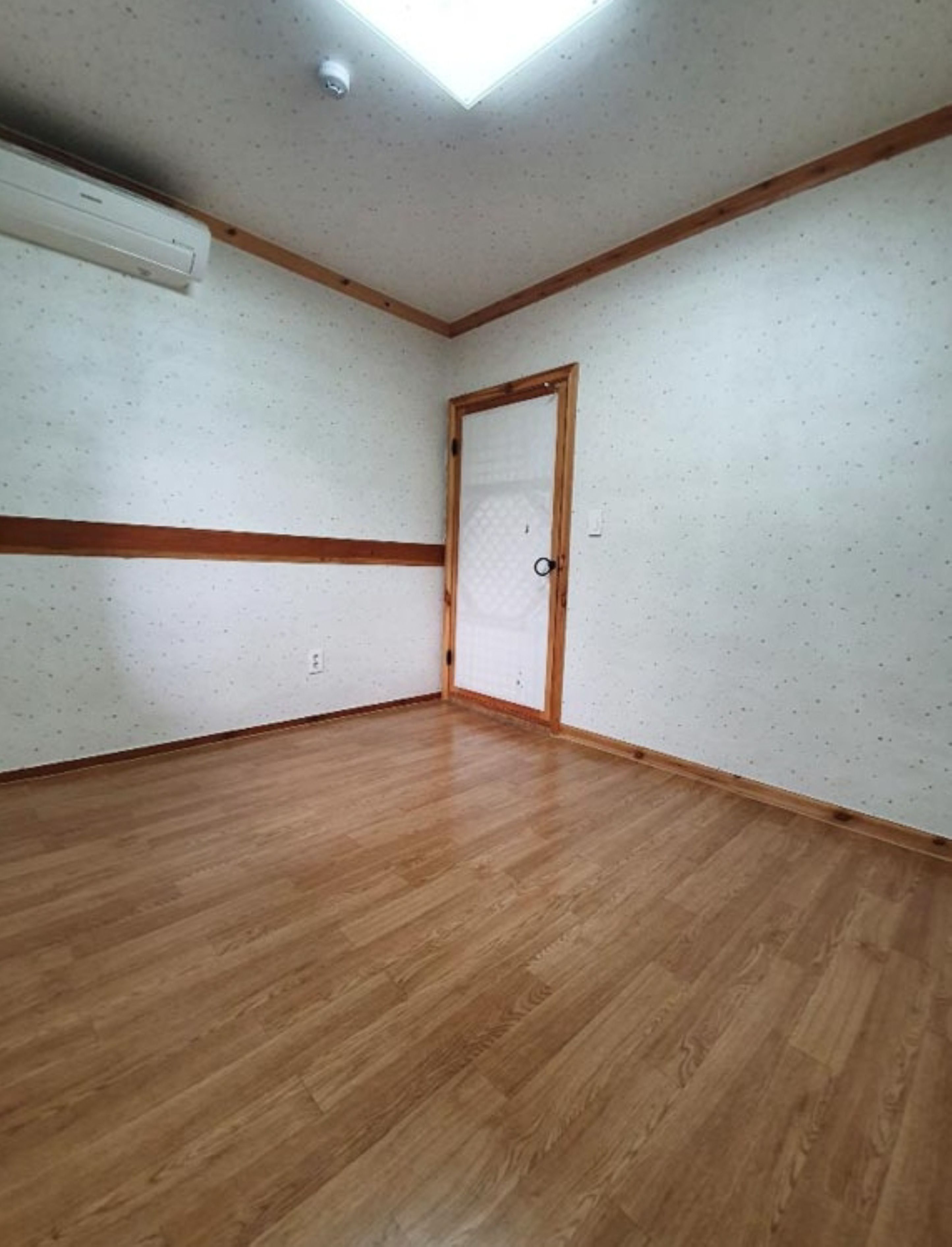 A room with wooden flooring, white walls, a skylight, and a door with a wooden frame.