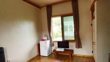Una habitación pequeña con piso de madera, una cama, un escritorio, una silla, una ventana con cortinas y un televisor.