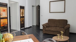 A living room with a brown sofa, a small wooden table with decorative items, and a wall-mounted picture frame. - Mini Apartments in Brindisi center Corso Garibaldi (Brindisi)