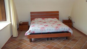 A bedroom with a wooden bed, a nightstand, a lamp, and a window with curtains.