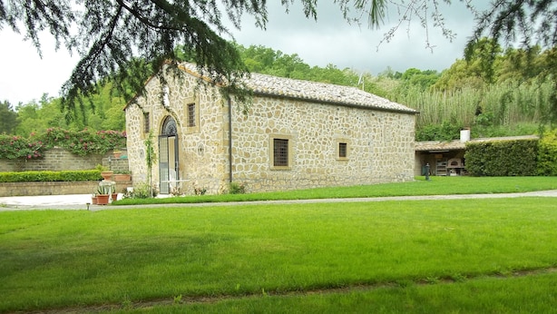 A stone building with a tiled roof, surrounded by a well-maintained lawn and flowering plants.