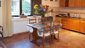 A dining area with a table and chairs, a window with curtains, and a kitchen area with wooden cabinets and a tiled backsplash.