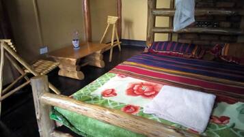 A rustic room with a wooden bed, a small wooden table, and a chair.
