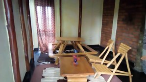 A room with a wooden dining table, two wooden chairs, a small wooden stool, and a cowhide rug. - Marianah Tourist Hotel (Mahyoro)