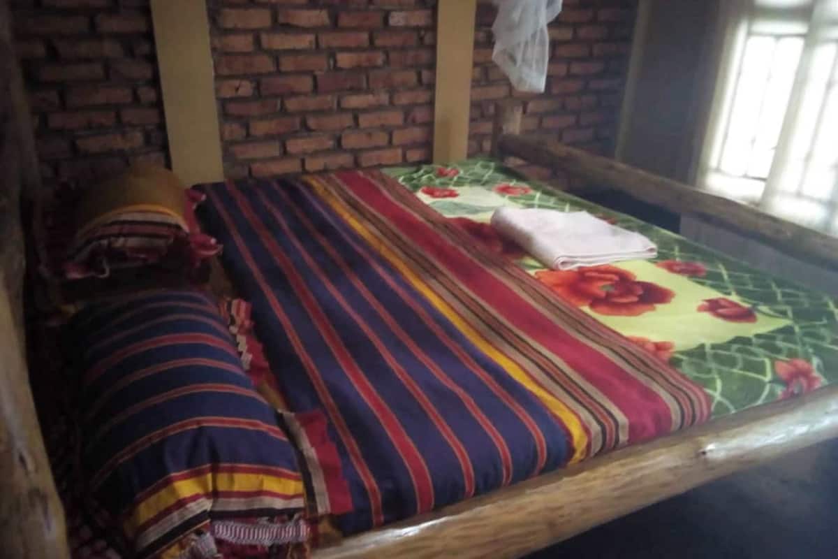 A single bed with a striped blanket and pillows, a floral bedspread, and a brick wall in the background.