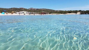 Une plage avec une eau claire et peu profonde, des parasols et des chaises de plage.