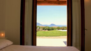 Une chambre avec une grande fenêtre, un lit et une vue sur un paysage verdoyant et des montagnes.