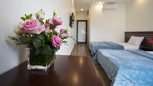 A hotel room with a bed, a bedside table with a vase of pink roses, and a hallway leading to another room. - Padama Hotel (Bai Chay)