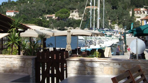 Ein Restaurant am Meer mit Außenbereich, Blick auf den Yachthafen und Gebäuden im Hintergrund.