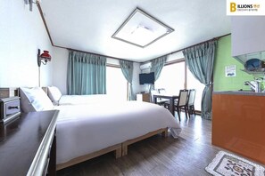 A hotel room with a bed, a desk, a chair, a television, and a kitchenette.