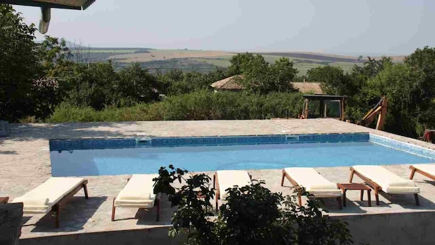 A swimming pool with lounge chairs, surrounded by greenery and a view of the countryside.