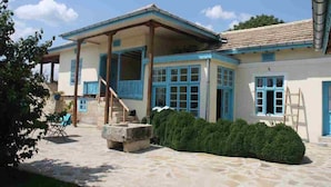 A two-story house with a covered patio, stone flooring, and a well-maintained garden.