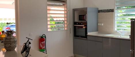 Una cocina moderna con armarios grises, horno empotrado y ventana con persianas.