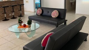 A modern living room with a black sofa, a glass coffee table, and a kitchen area in the background. - F3 FROM 2 TO 6 BEDS 10 MN BEACH BOURG DE SAINTE ANNE (SAINTE ANNE)
