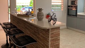 A modern kitchen with a central island, bar stools, a bicycle, and a view of greenery outside. - F3 FROM 2 TO 6 BEDS 10 MN BEACH BOURG DE SAINTE ANNE (SAINTE ANNE)