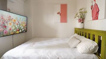 A bedroom with a bed, a wall-mounted air conditioner, a floral painting, a pink accent wall, and a framed illustration.