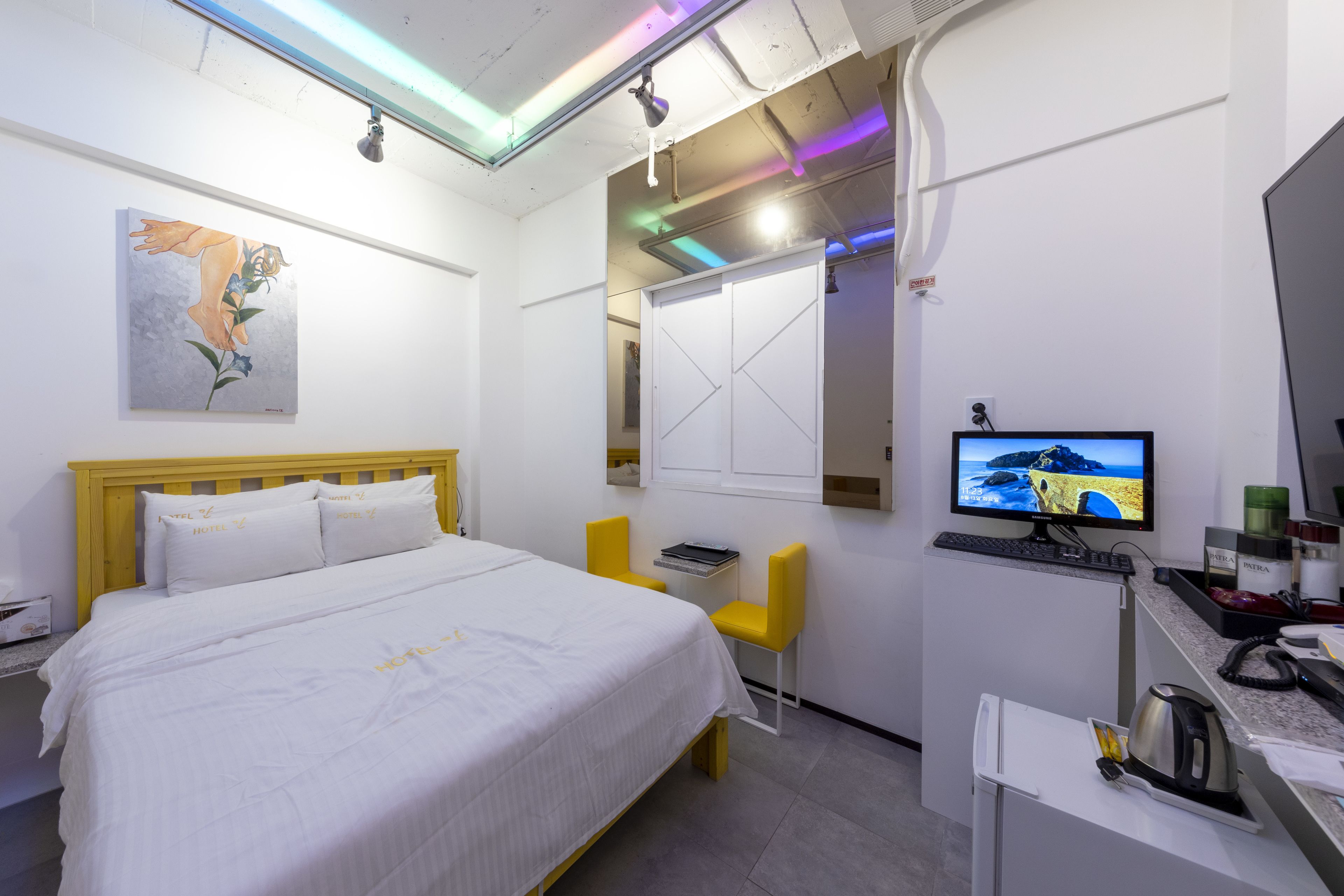 Quarto de hotel com cama, escrivaninha, cadeira, televisão e um quadro na parede.