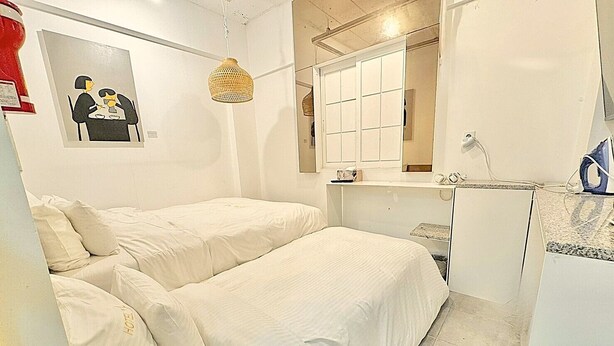 Habitación de hotel con dos camas, una kitchenette pequeña, un espejo y una lámpara colgante.