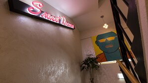 Un letrero de neón que dice 'Sweet Dreams' en un pasillo con una escalera y un cuadro de colores en la pared.