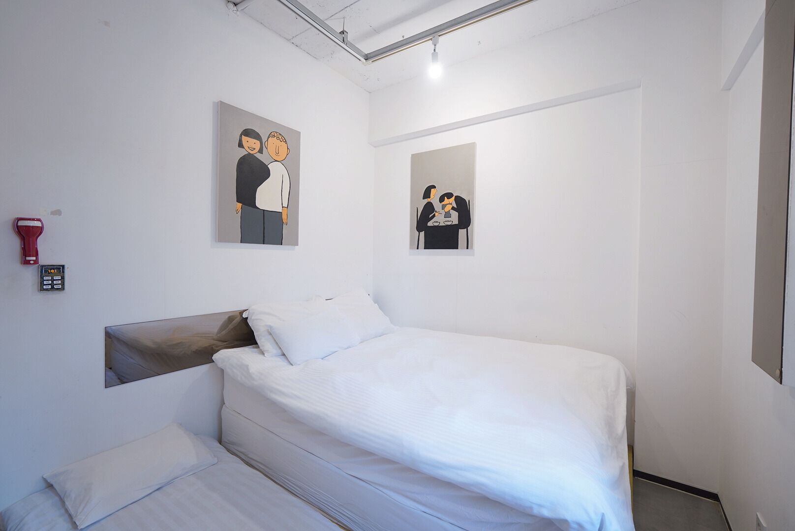 A bedroom with a bed, a headboard, a wall-mounted alarm clock, and two framed artworks.