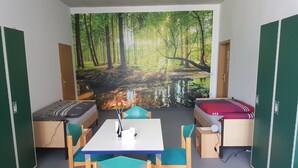 A room with a bed, a desk, and a chair. There is a mural of a forest on the wall. - Hostel jo-si (Kamenz)