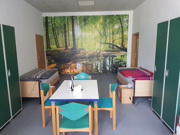 A room with a bed, a desk, and a chair. There is a mural of a forest on the wall.