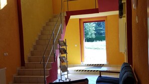 A spacious living area with a staircase leading to an upper floor, a sofa, and a small table. - Hostel jo-si (Kamenz)