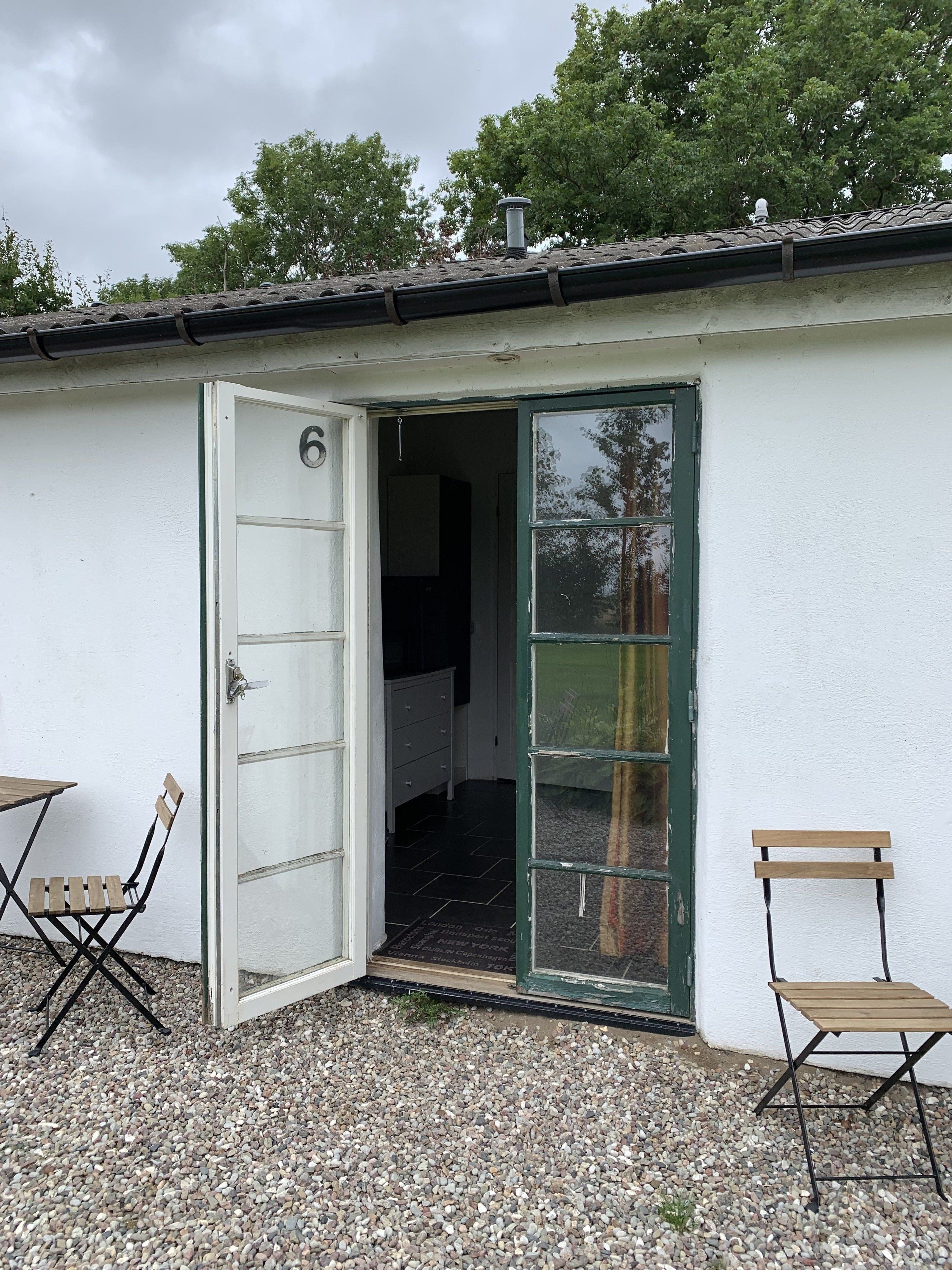 Un xalet petit, d'una sola estança, amb façana blanca, porta verda i una finestra petita.