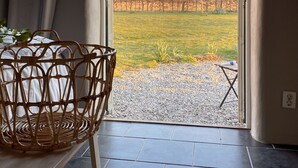 Una habitación con una silla de mimbre, una mesita y vistas a un jardín exterior a través de un ventanal.