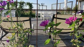 Un espace jardin agrémenté d’une clôture en métal, d’une terrasse en bois et de chaises blanches.
