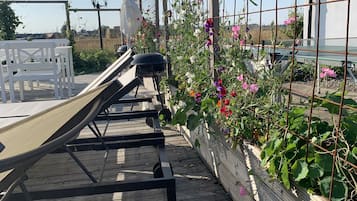 Una terraza de madera con equipo de ejercicio, una cerca blanca y un jardín con diversas plantas y flores.