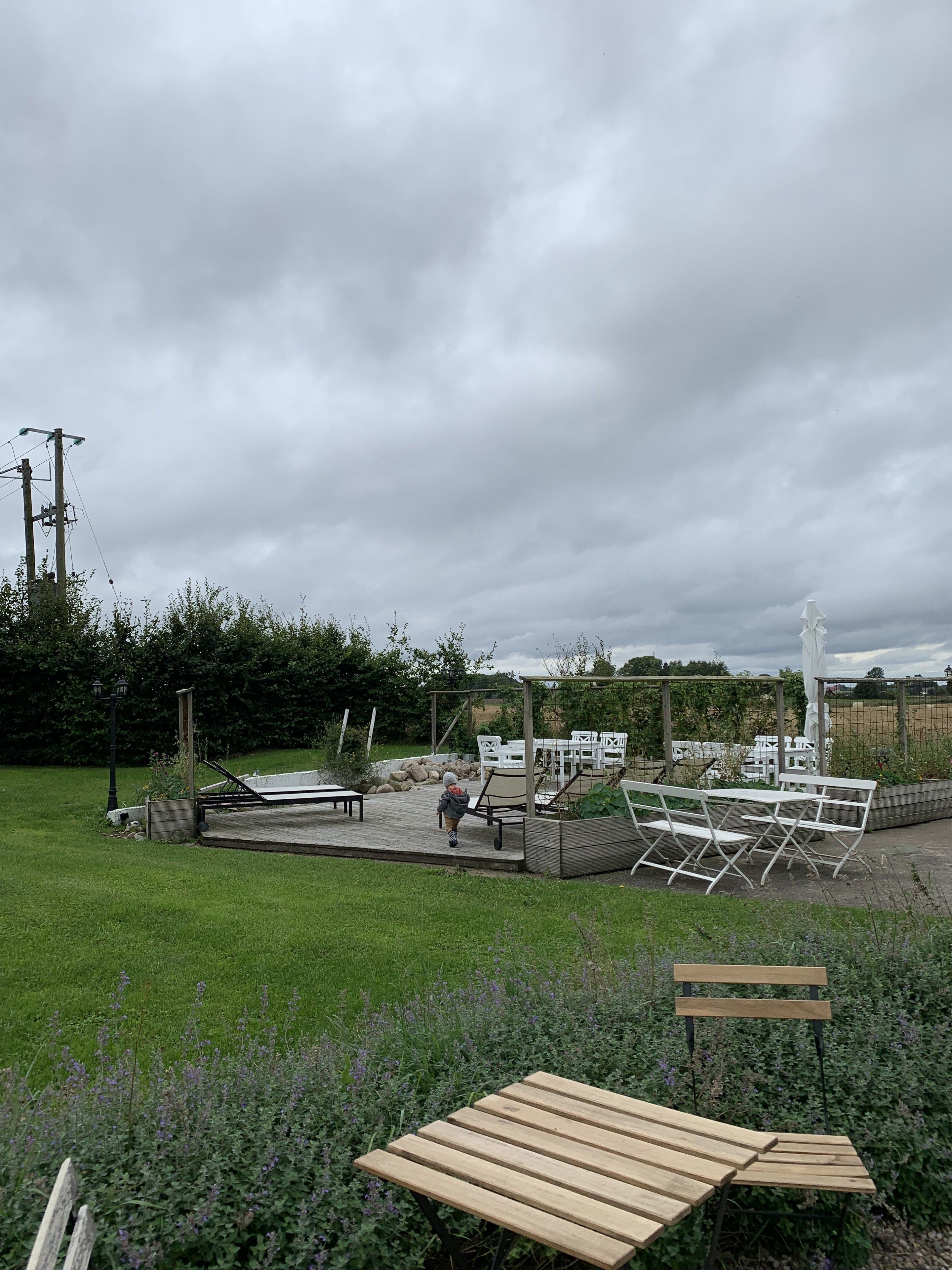 An outdoor area with a wooden deck, white plastic chairs, and a table.