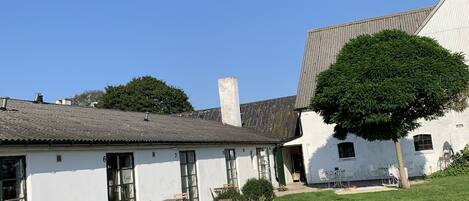 A white building with a sloped roof, a chimney, and a small garden area with grass and shrubs.