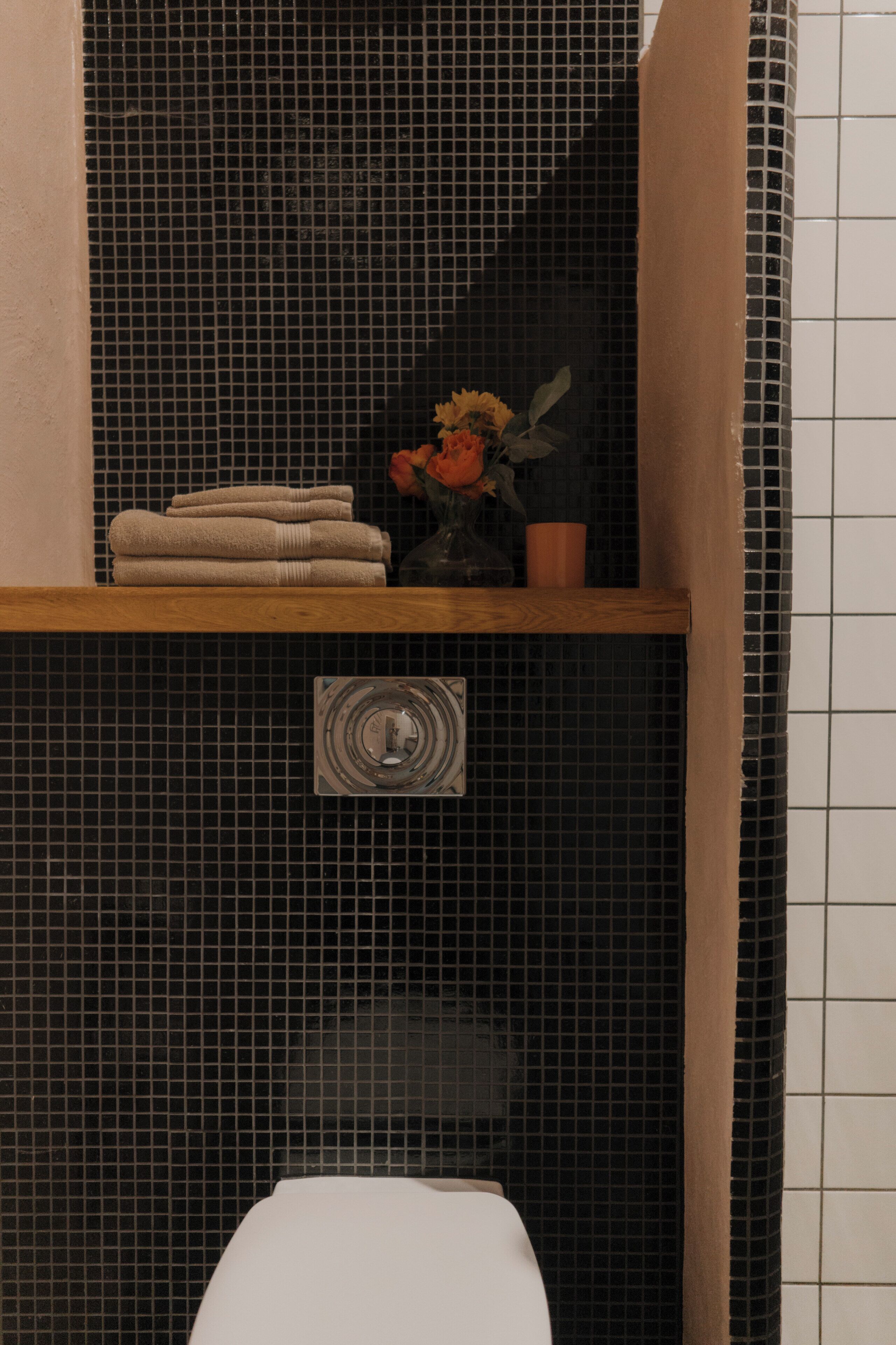 Ein Badezimmer mit schwarzem Fliesenbelag, einem Holzboden mit Handtüchern, einer kleinen Topfpflanze und einer Toilette.