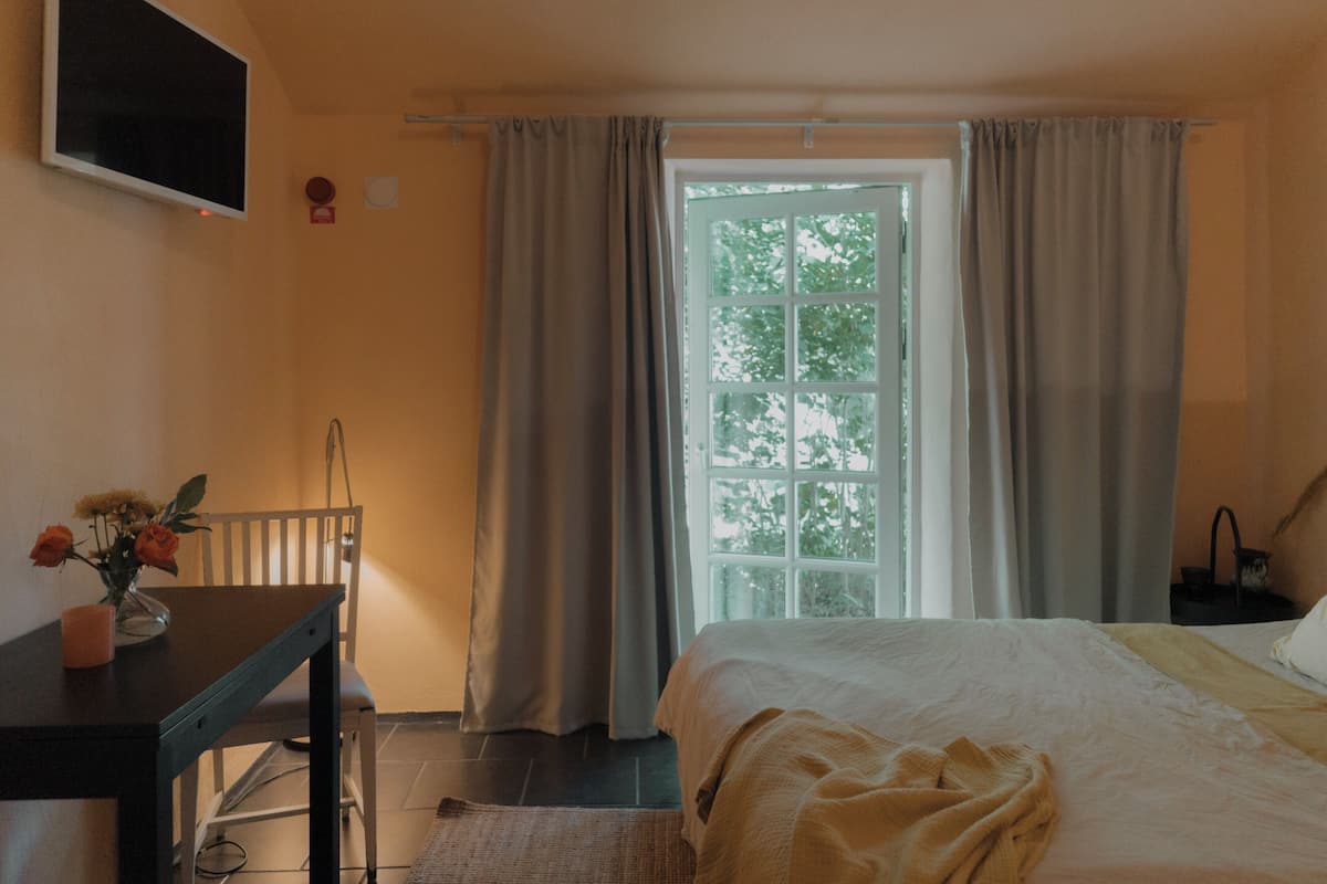 A bedroom with a bed, a desk with a vase of flowers, a chair, and a window with curtains.