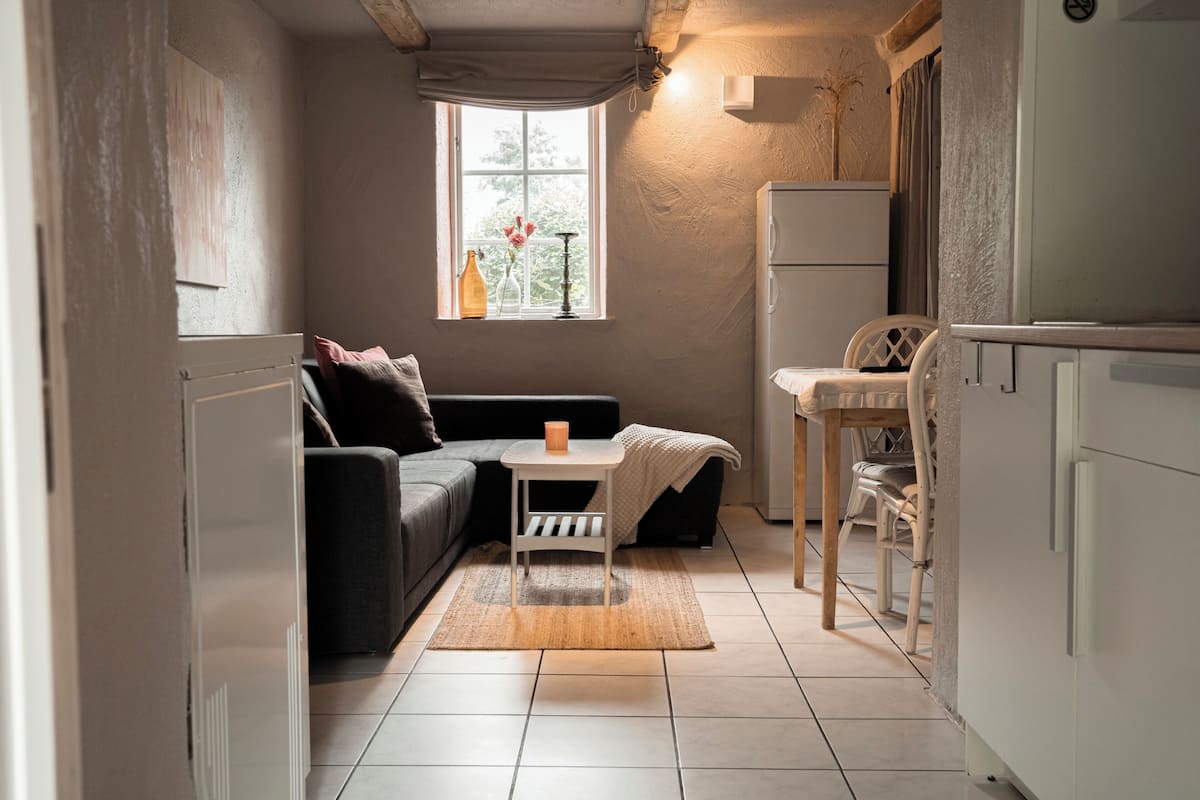 A compact living space with a kitchenette, a sofa, a small table, and a window with a view.