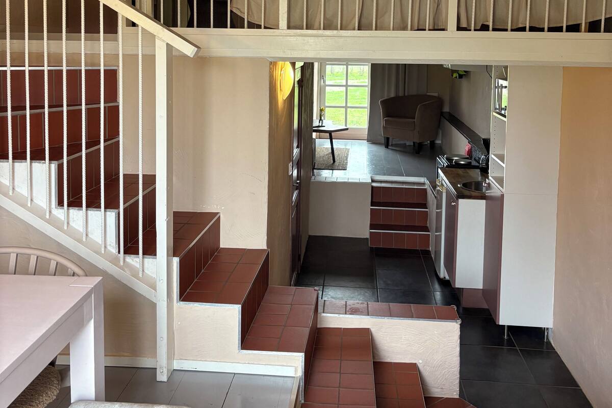 A multi-level interior with a staircase, a kitchen area, and a bed with a view.