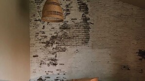 Un dormitorio con pared de ladrillo, lámpara colgante, cama con varios almohadones y mesita de noche con una vela.