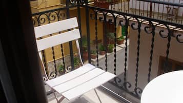 Un balcon avec un banc blanc, des plantes en pot et une vue sur la rue en contrebas.