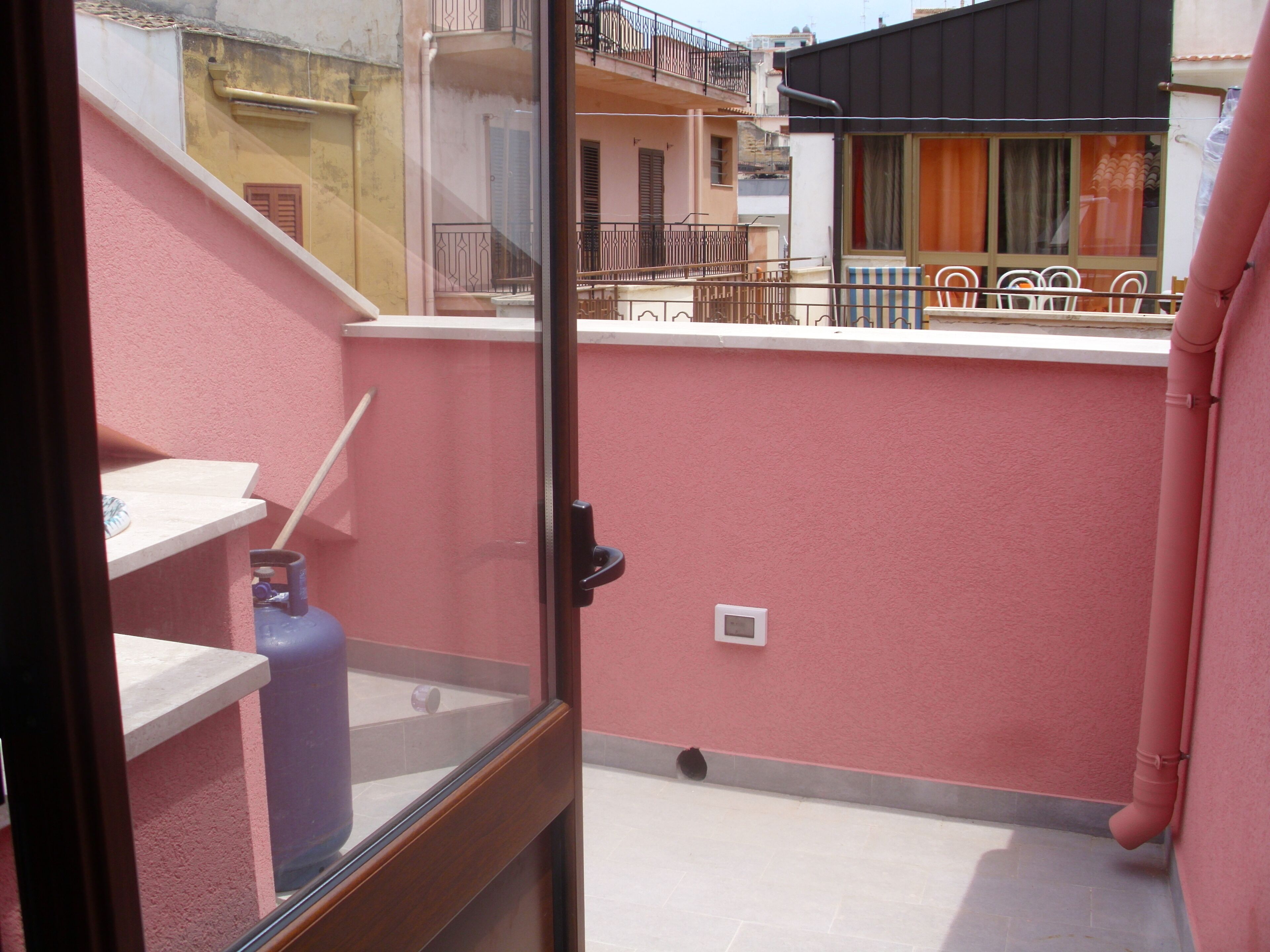 Un balcon avec un mur rose, une fenêtre et une rambarde en métal.