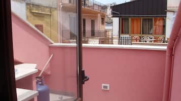 Un balcon avec un mur rose, une fenêtre et une rambarde en métal.