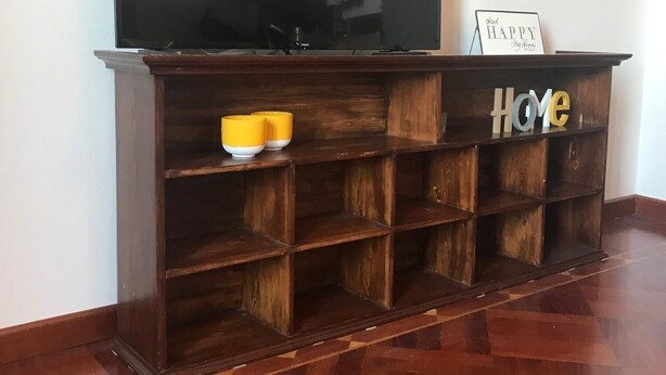 Ein Holzunterhaltungsmöbel mit einem Flachbildfernseher, einer kleinen Ablage mit einer Schale und einem Schild mit der Aufschrift 'Thank Happy My Happy'.